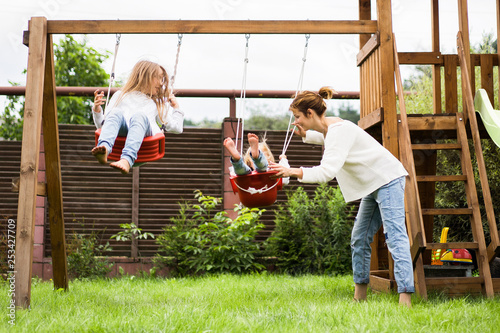 children on the swing. girls sisters swinging on a swing in the yard. summer fun.