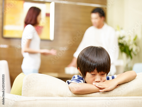 unhappy child with fighting parents in background