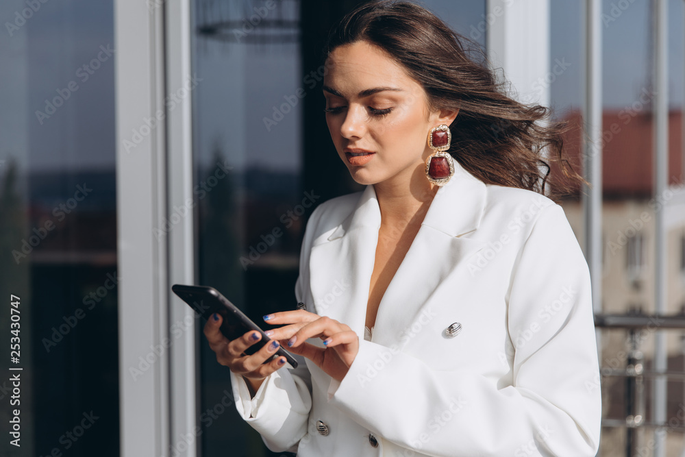 Pretty stylish business woman stands on the balcony near modern office and talking on the smartphone. Pretty stylish business woman stands on the balcony near modern office and talking on the smartphone.
