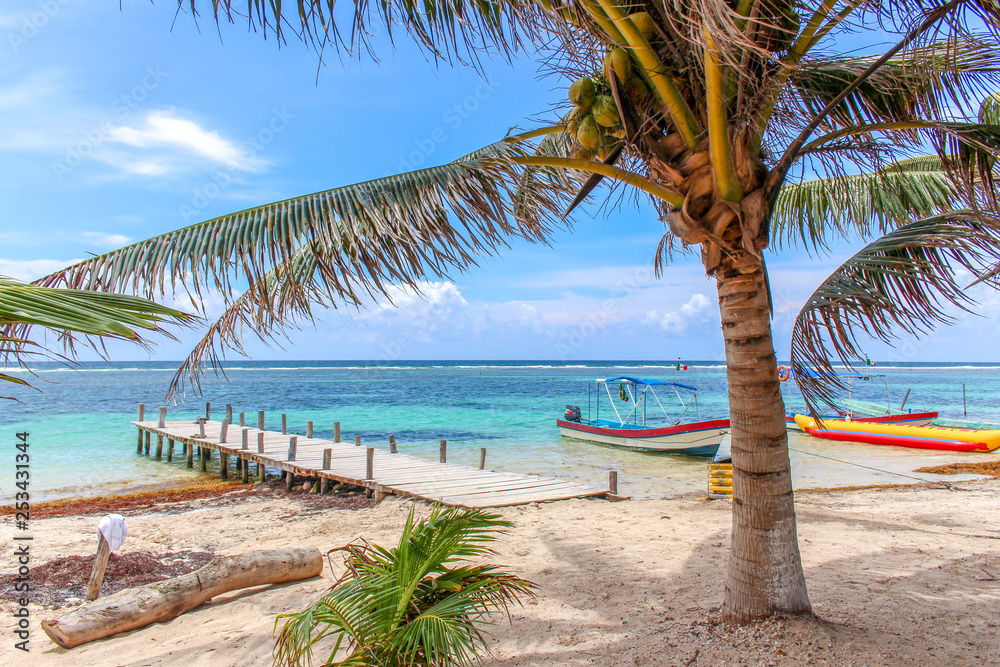 Obraz premium Beautiful tropical beach with turquoise water, a pier and a colorful boat at Mahahual, Mexico