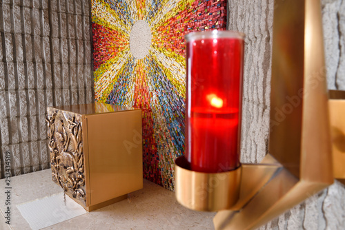 Red Sanctuary Lamp or Eternal Flame at the Tabernacle with bronze Lamb of God bas relief at side altar with sunburst mosaic in Catholic church
