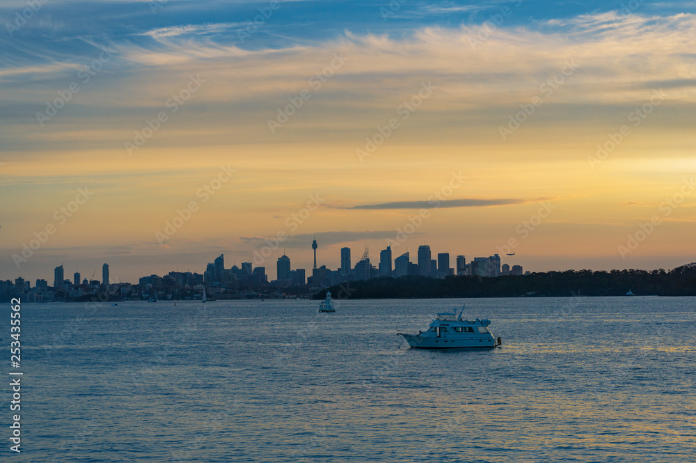 Fototapeta premium Colourful sunset over harbour with yachts and Sydey cityscape in the distance