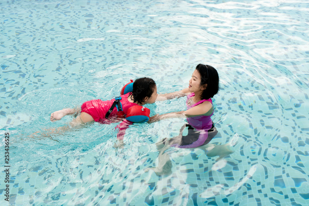 Top view of Asian Mother and child swimming in the pool. Happy mother teaching her daughter to swim. Little child learning and exercising in the water.