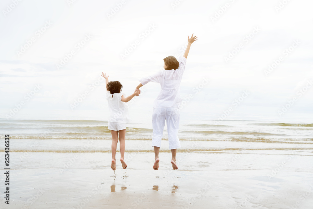 Relaxing Asian family time during summer vacation. Asian Mother with daughter holding hands, having fun and jumping on beach.