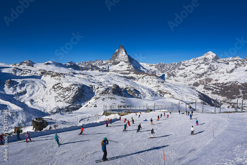 Skiers skiing downhill at Gornergrat with Matterhorn view in background.