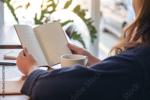Closeup image of a woman holding and opening a blank notebook with coffee cup and papers on the table