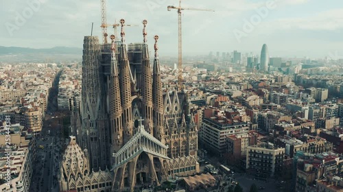 Aerial; drone view of main Barcelona attraction; majestic building towering over the rooftops of Eixample; sharp domes and unusual forms of great unfinished work of neo-gothic art; camera moves around