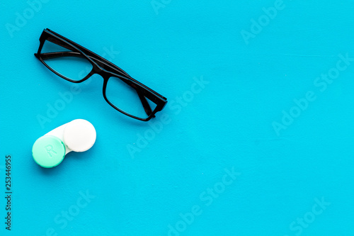 Eye problems. Glasses with transparent lenses and contact lenses on blue background top view copy space