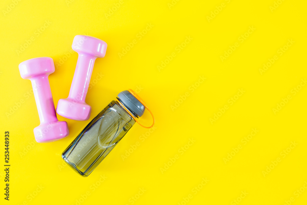 Top view of pink dumbbells and bottle of water on yellow background. Fitness and Healthy lifestyle background concept. Top view of pink dumbbells and bottle of water on yellow background. Fitness and Healthy lifestyle background concept.