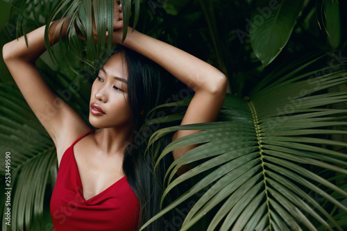 Fashion. Asian woman model in red dress with green palm leaves