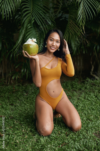 Summer fashion. Girl in swimsuit with coconut drink in nature