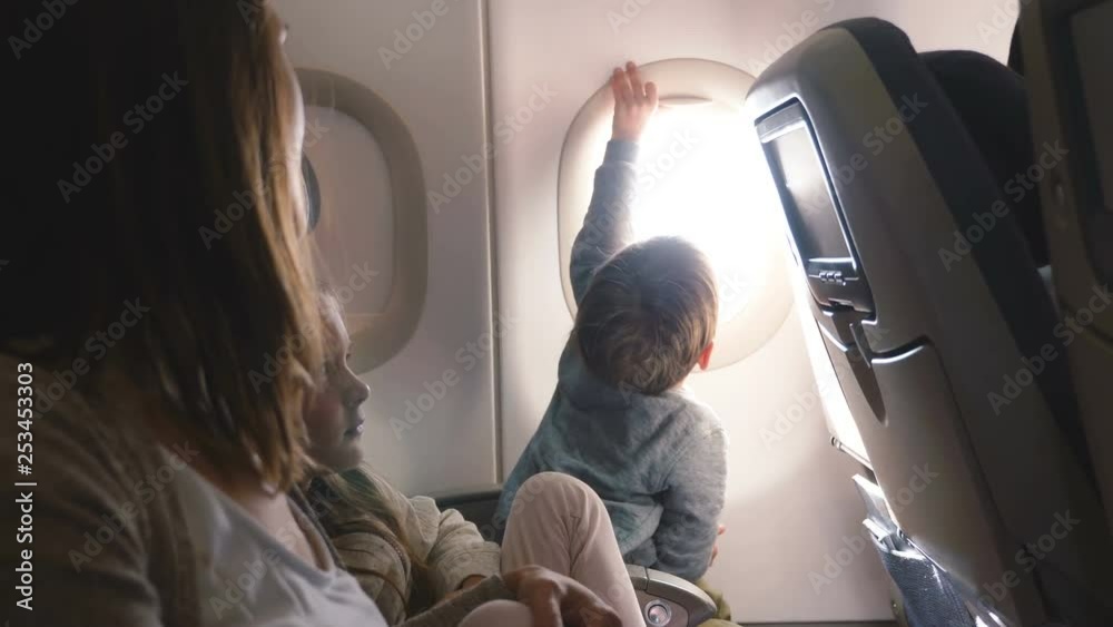 Happy curious little boy opening airplane window cover during flight, enjoying the view going to vacation with family.