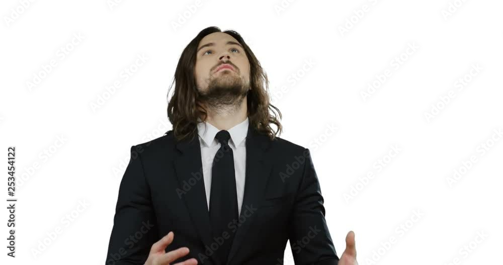 Caucasian handsome young man with long hair in the suit and tie standing on the white background and playing with a football ball in his hands. Caucasian handsome young man with long hair in the suit and tie standing on the white background and playing with a football ball in his hands.