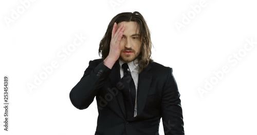 Portrait shot of the handsome young Caucasian man with long hair in the suit and tie looking very tired while standing on the white background. photo