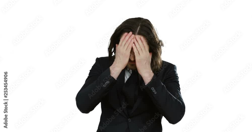 Portrait shot of the upset young Caucasian man with long hair in the suit and tie looking desperate as failed while standing on the white background. Portrait shot of the upset young Caucasian man with long hair in the suit and tie looking desperate as failed while standing on the white background.