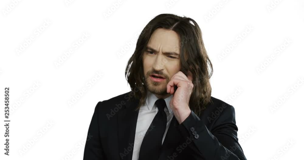 Close up of the young angry serious man in the black suit calling and screaming while talking on the phone on the white wall background. Close up of the young angry serious man in the black suit calling and screaming while talking on the phone on the white wall background.