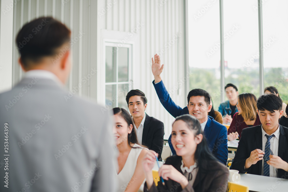 Obraz premium Asian male speaker is speaking at seminars and workshops to the people in the meeting. Participants are raising their hands to ask questions.