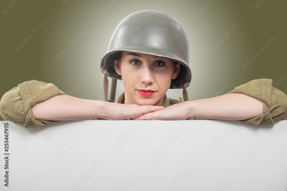 young woman dressed in wwii military us uniform with helmet showing empty blank signboard with a copyspace young woman dressed in wwii military us uniform with helmet showing empty blank signboard with a copyspace