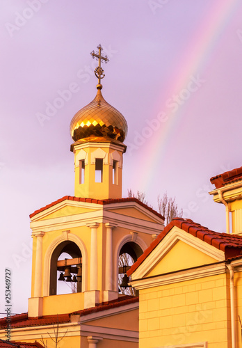 The golden domes of the Orthodox Christian church in the rays of the evening sun setting against the background of a bright multi-colored rainbow after the rain. Rainbow, Good News, Gospel
