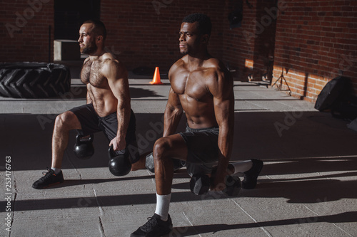 Focused male african and caucasian athletes showing determination and endurance exercising legs and back musculs during body core crossfit workout photo