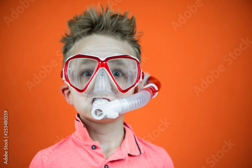 funny boy in swimming goggles and snorkel on bright orange background © mikitiger
