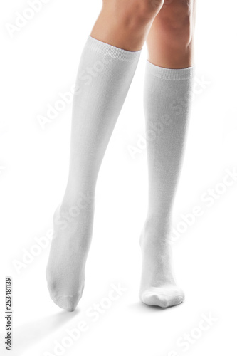 Cropped front shot of woman's slender legs wearing snowy knee high socks. The girl is making a step against the white background. Comfortable legwear for ladies and girls. Stylish women's hosiery.