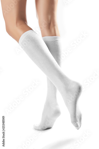 Cropped half-turn shot of girl's slender legs wearing snowy knee high socks. The woman is making a step against the white background. Comfortable legwear for ladies and girls. Trendy women's hosiery.