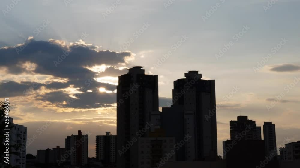 Suns ray bleeding light leaks through fast moving cloud timelapse behind skyscraper building on horizon. Suns ray bleeding light leaks through fast moving cloud timelapse behind skyscraper building on horizon.