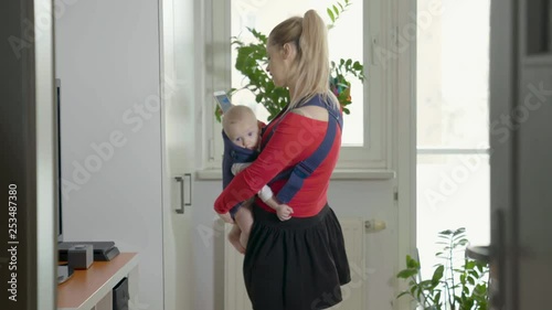 A young pretty mom is carrying her little boy in a baby carrier.