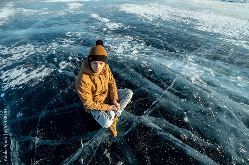 Tourist traveler meditates sitting in Lotus position on the ice of lake Baikal