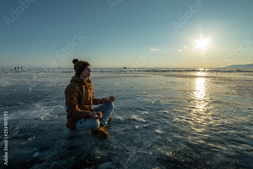 Tourist with a backpack meditates sitting in Lotus position on the ice of lake Baikal. Relaxation and freedom of nature