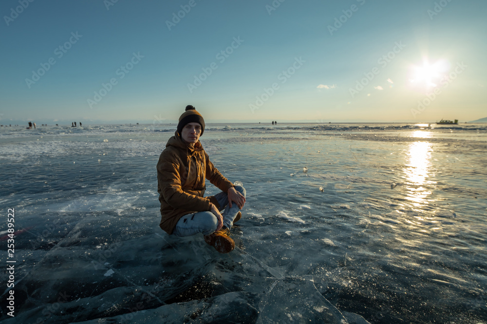 Fototapeta premium Tourist with a backpack meditates sitting in Lotus position on the ice of lake Baikal. Calm and freedom of nature