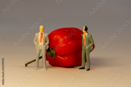 Two miniature business men in suit standing in front of the red hot Habanero pepper. Business conflict concept photo