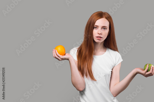 serious slim girl in white T-shirt holding an orange and apple.diet concept, body care. woman leads healthy lifestyle