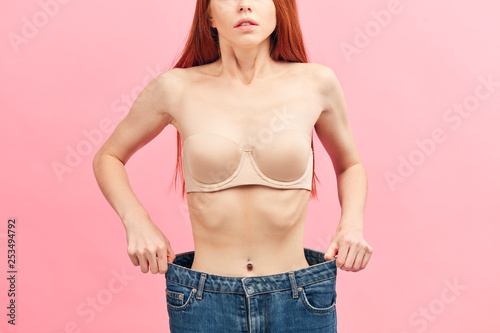 Concept of dieting with oversized jeans, Midsection shot of skinny thin female body in underwear with protruding ribs shows her results of long-term abstaining from food close up