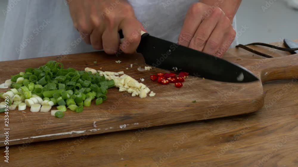 Slicing fresh hot chillies on a board among celery and garlic in preparation to cook Slicing fresh hot chillies on a board among celery and garlic in preparation to cook