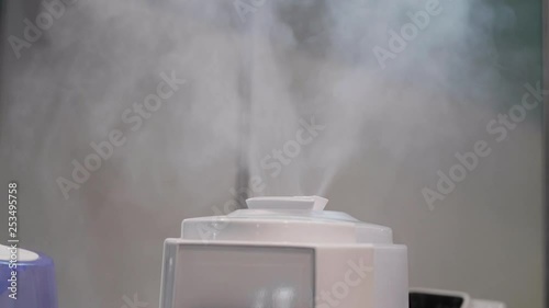 Air humidifier spreading steam with a lot of vapor volume indoor. Steam from white air moistener distributing fume in the room. Electric humidifier and oil diffuser working indoors. Humidification photo