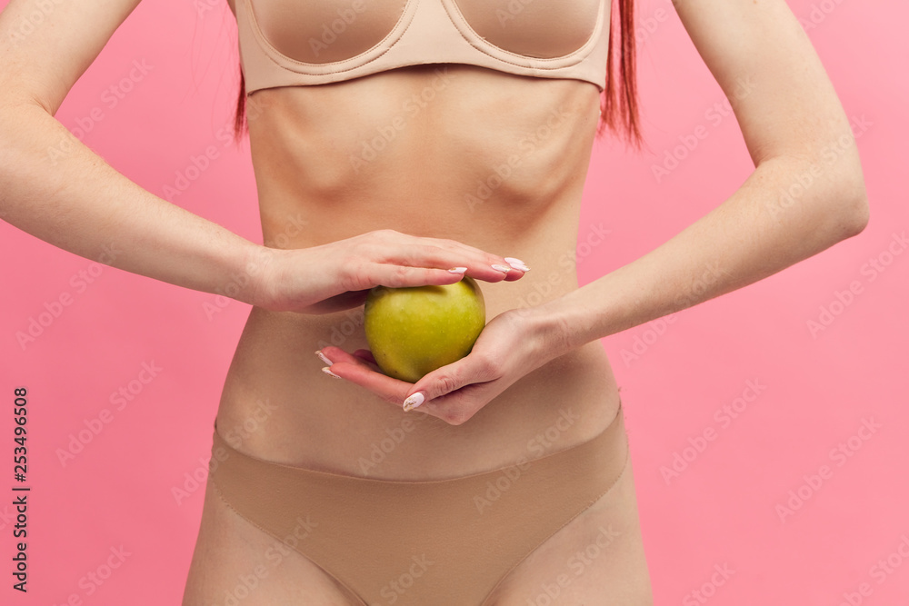 Midsection portrait of female thin skinny body in nude underwear, holding  green apple for wellness, weight loss and healthy isolated on pink  background, healthcare and diet concept. Photos
