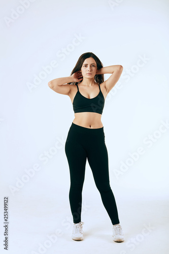 Attractive red-haired woman in black sportswear posing on white background