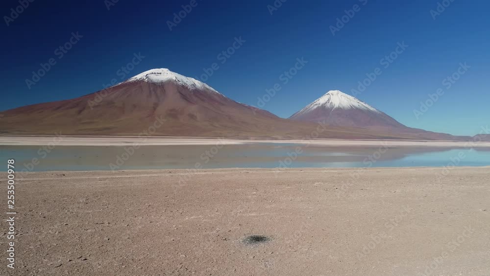 Aerial panoramic view of Laguna Verde/Blanca, snowy peaks of volcanos Licancabur and Juriques reflecting on lake, sunny day with blue sky - landscape of Atacama desert, Andes, Bolivia, South America Aerial panoramic view of Laguna Verde/Blanca, snowy peaks of volcanos Licancabur and Juriques reflecting on lake, sunny day with blue sky - landscape of Atacama desert, Andes, Bolivia, South America