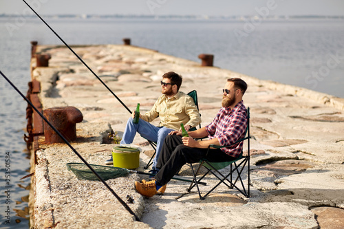 leisure and people concept - happy friends fishing and drinking beer on pier © Syda Productions