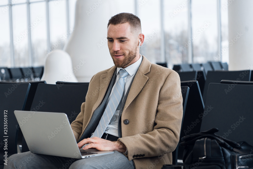 Happy businessman working on the laptop at the airport waiting lounge. Handsome caucasian businessman at waiting room in airport terminal Happy businessman working on the laptop at the airport waiting lounge. Handsome caucasian businessman at waiting room in airport terminal
