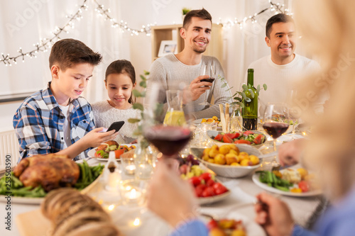 technology, holidays and people concept - happy children with smartphone at family dinner party