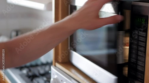 Man places leftover meal in a white bowl into a microwave oven and sets the timer. He then closes the door and starts the appliance.