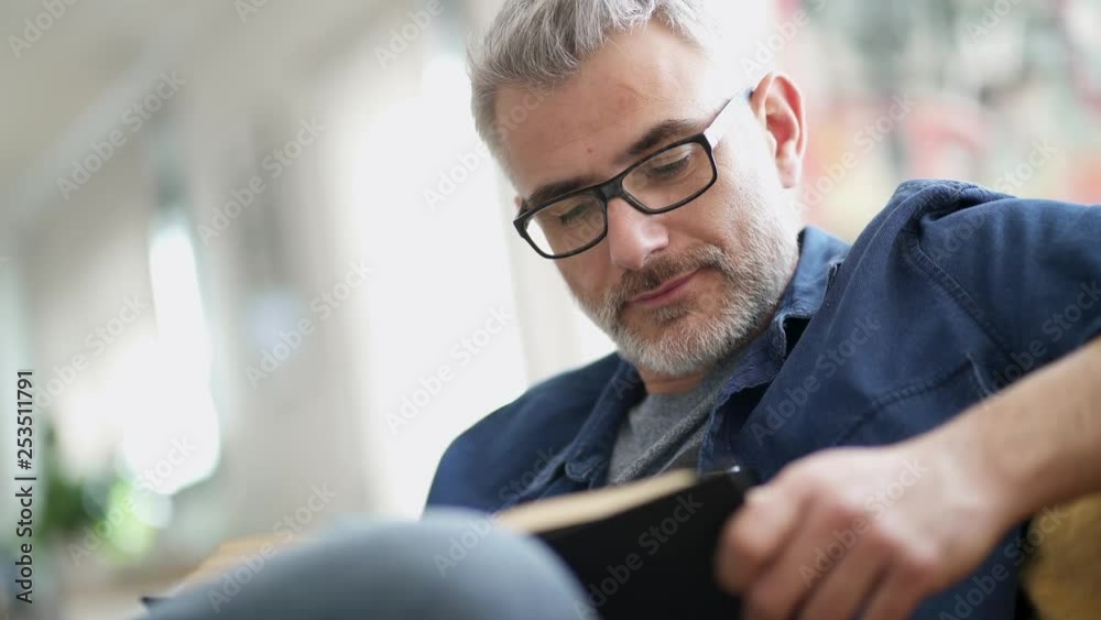 Mature man wearing glasses reading book at home
