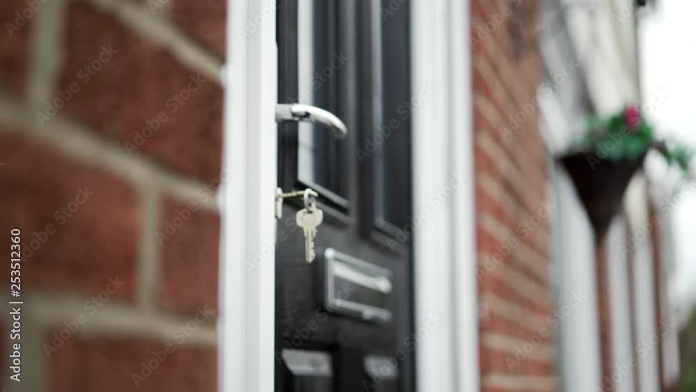 House keys left in black front door, red brick and white framed residence.