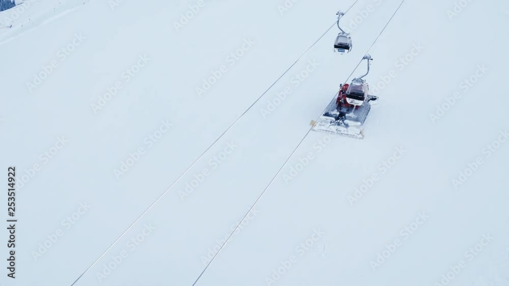 Aerial of two snowcats are going uphill while the gondola passes above them. Aerial of two snowcats are going uphill while the gondola passes above them.
