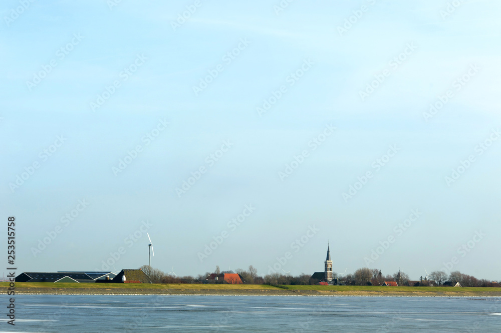 Ice on water in front of distant city in Netherlands. View on old church, houses and windmill. Free copy space.