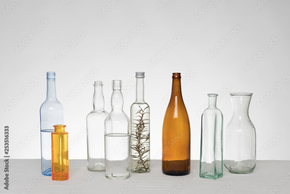 Fototapeta premium Verschiedene Glasflaschen vor weißem Hintergrund auf Tischdecke aus Leinen