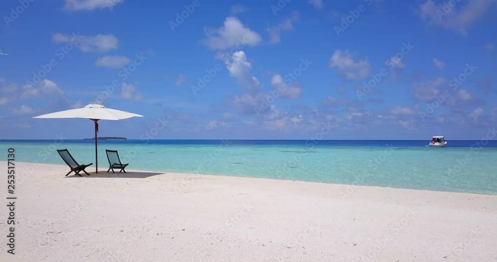 Tranquil scene with empty sun chairs on crisp white beach. Boat with people rocking in clear turquoise water. Slow flythrough secluded environment.